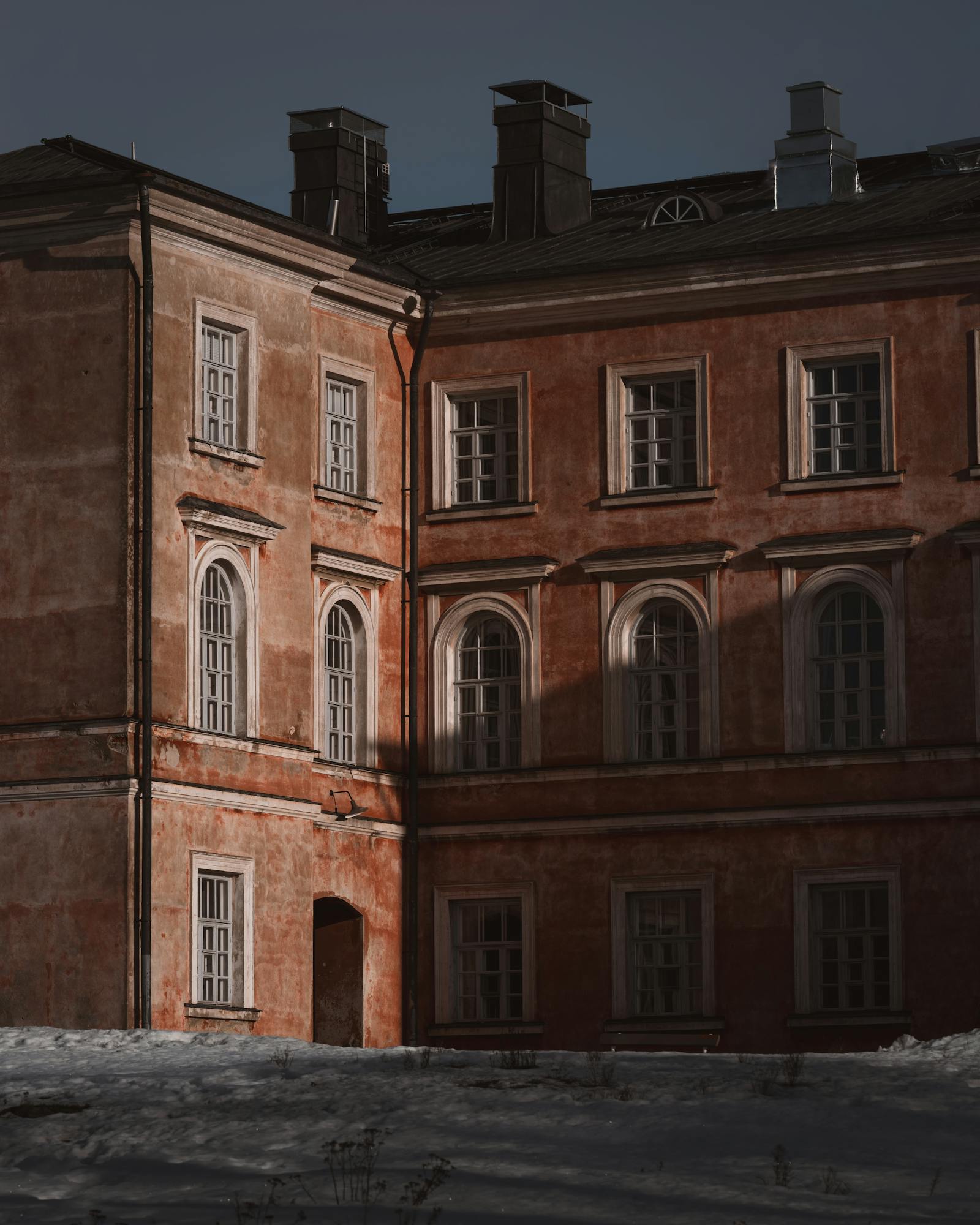 A vintage Helsinki building in winter with snow and warm tones, highlighting architectural details.