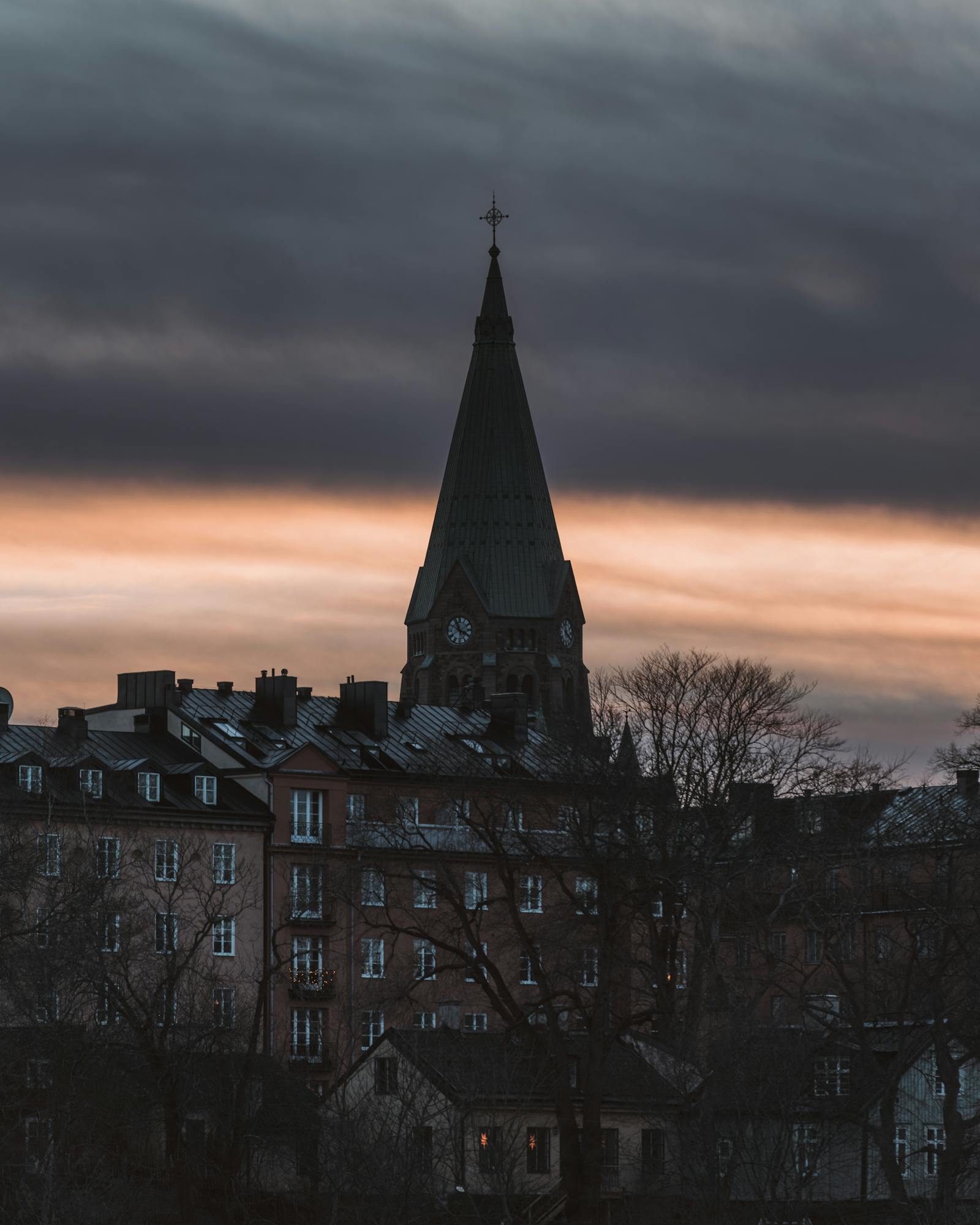 Silhouette of a church tower against a moody sky at dusk in an urban setting.