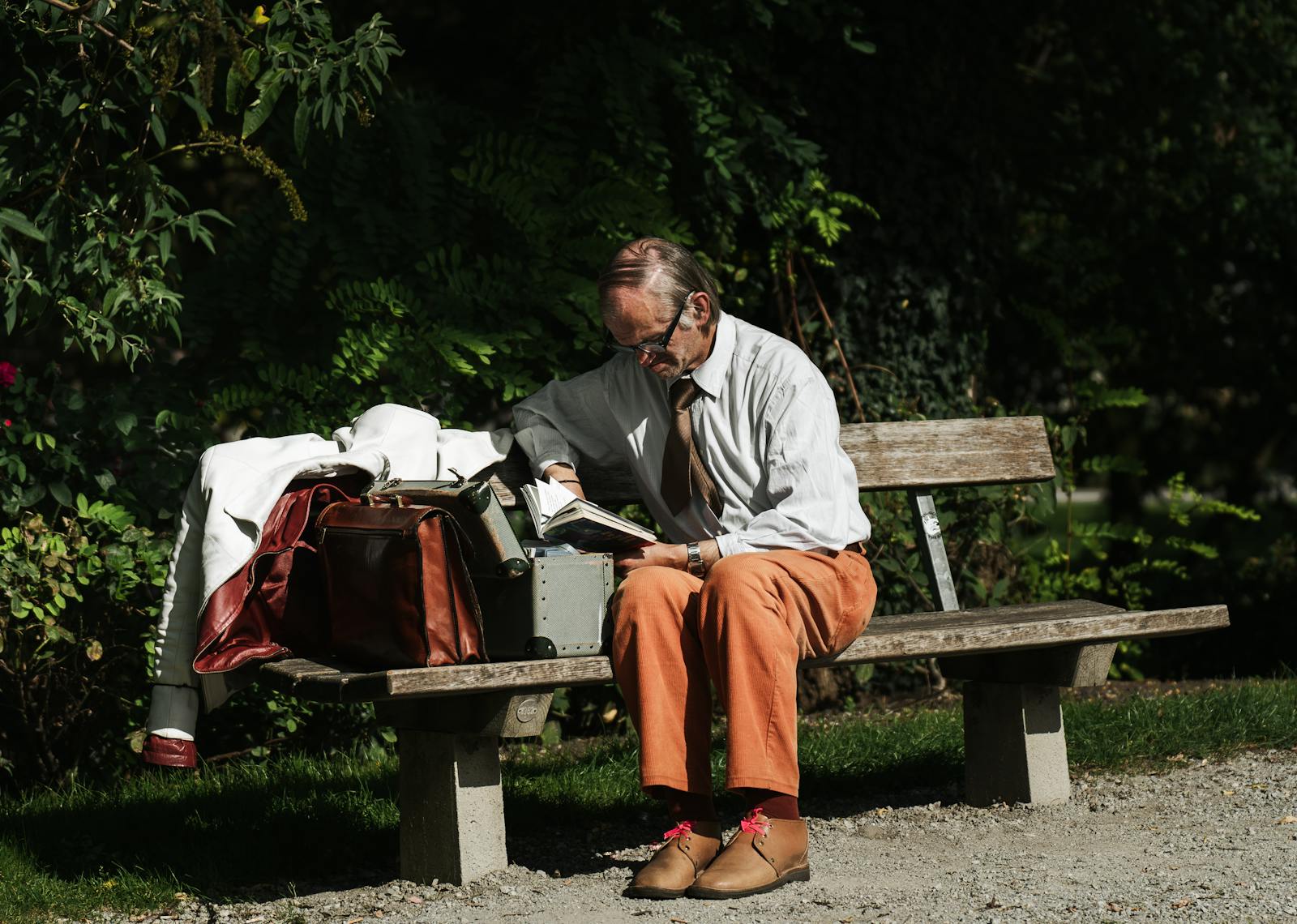 Senior man reading outdoors in a Salzburg park, with luggage and jacket on bench.