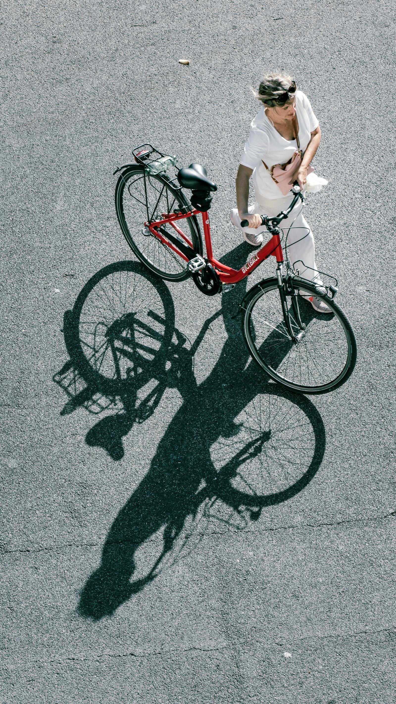 A woman walking her red bicycle on the streets of Rome, casting a distinct shadow.