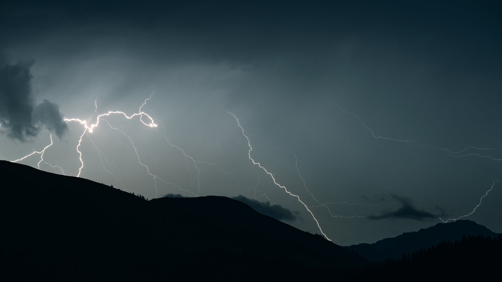 Captivating shot of lightning illuminating a dark sky over mountain silhouettes during a thunderstorm.