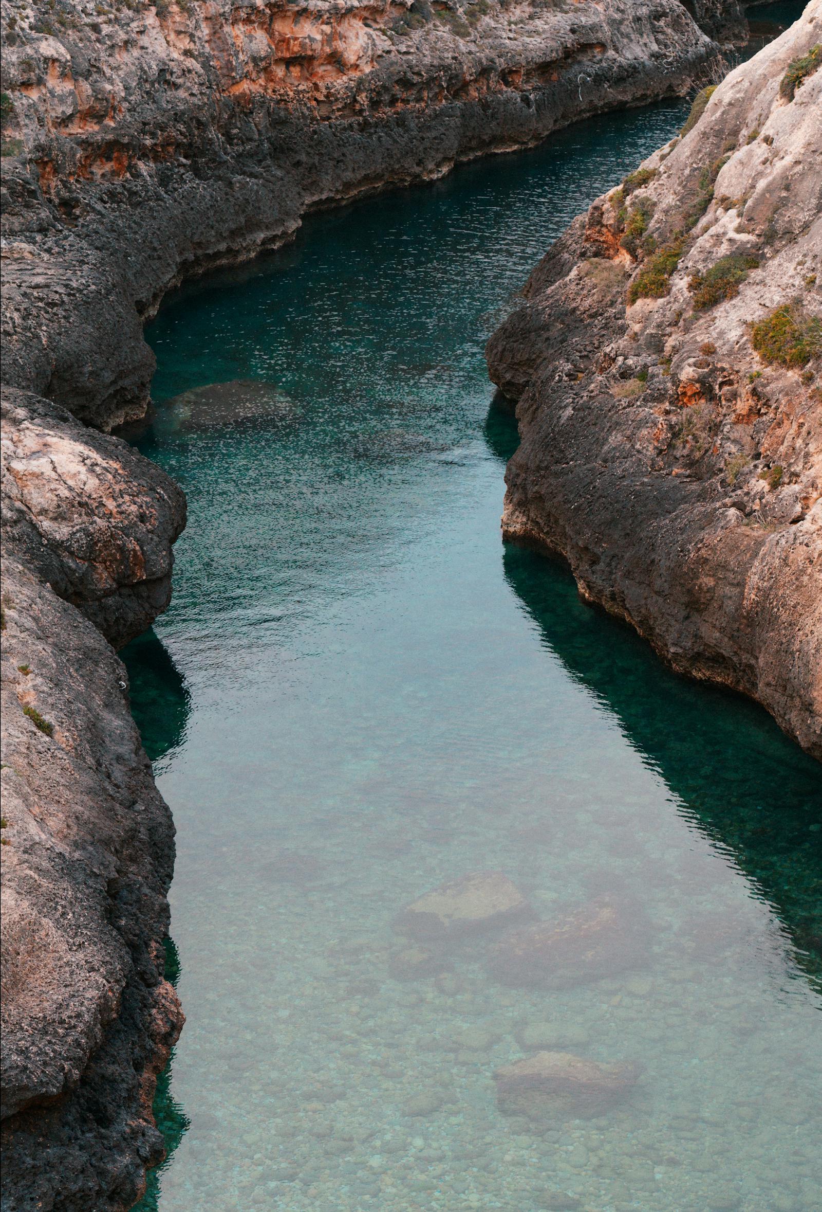 A tranquil view of a gorge with crystal-clear water surrounded by rocky formations.