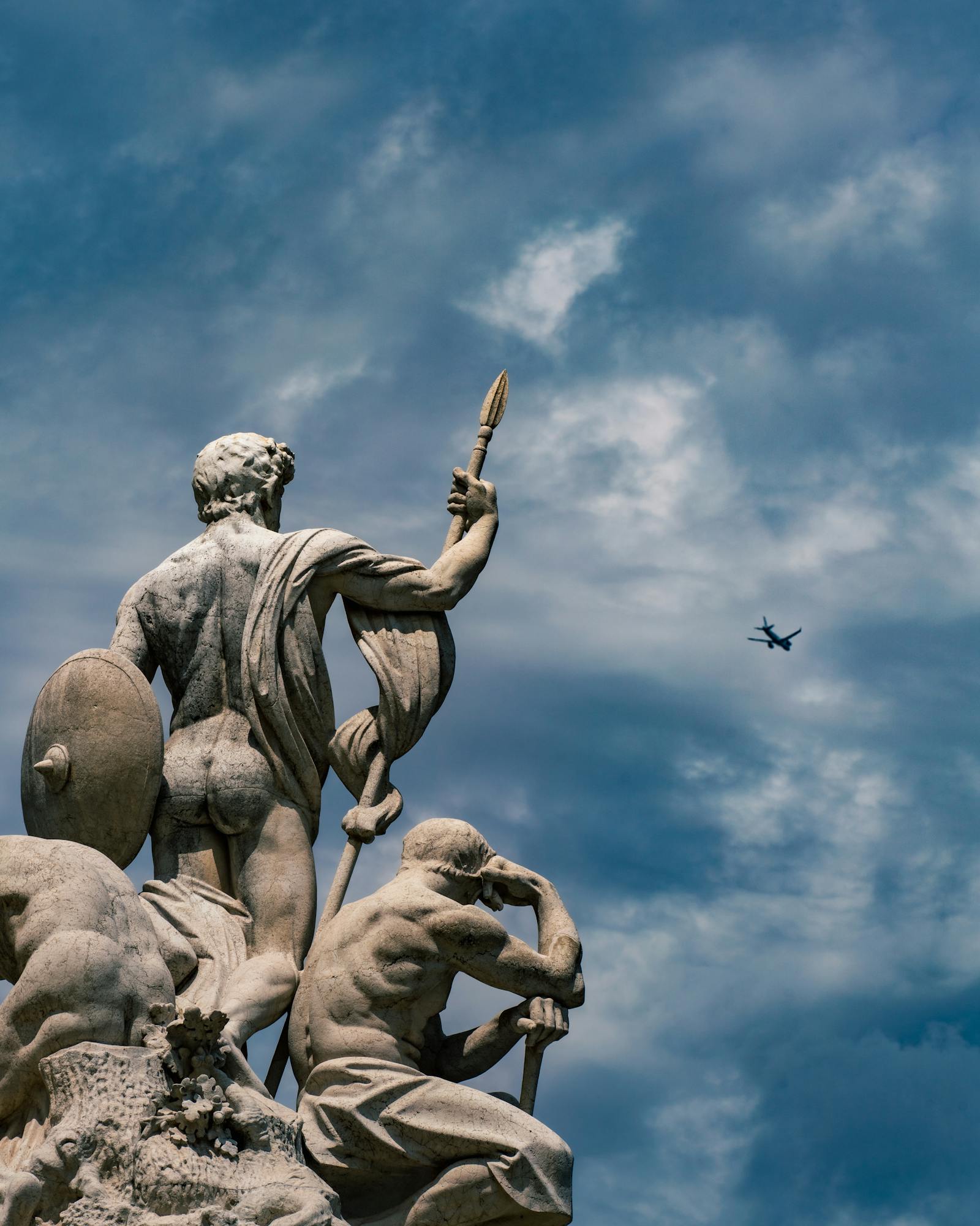 Statue in Rome, Italy, with a plane in the sky. Captures classic artistry and modern travel.