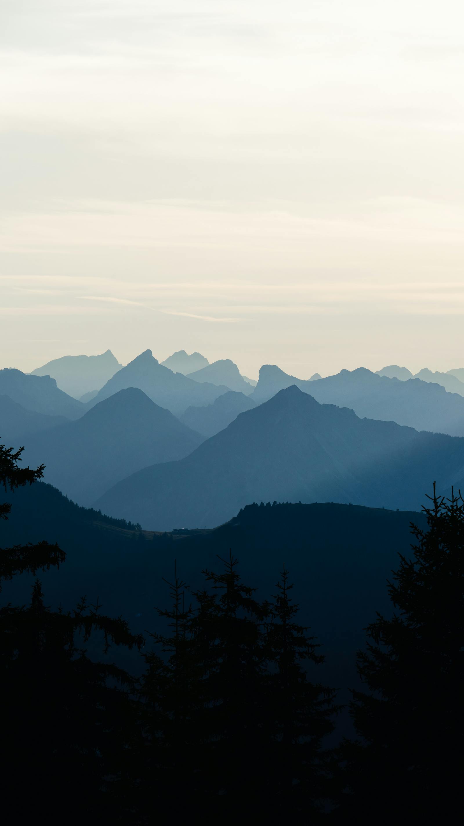 Scenic aerial view of the Tyrolean mountain range silhouetted against a dawn sky, capturing layers of peaks and soft light.