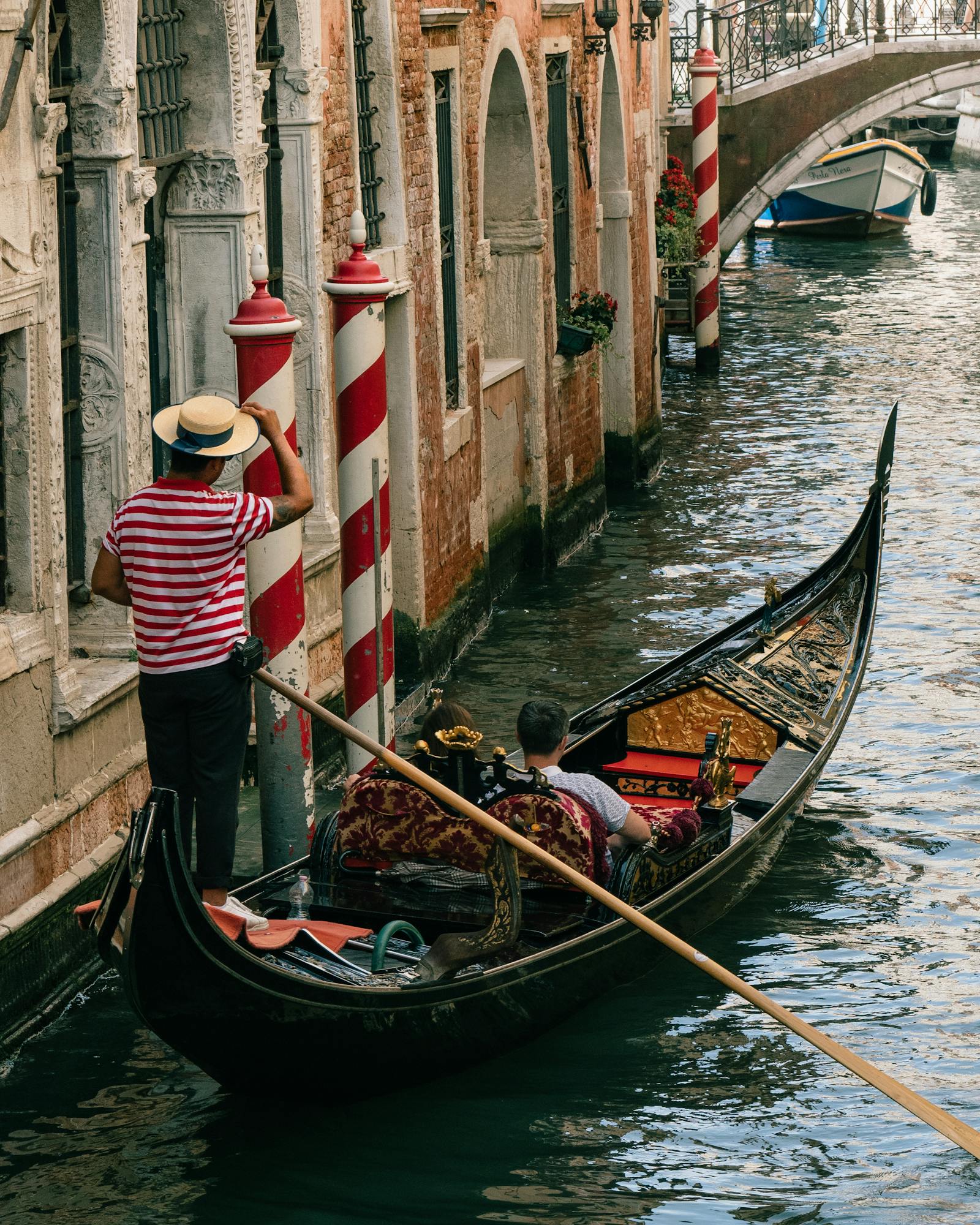 Gondolier navigating a couple in a gondola along a scenic Venetian canal.