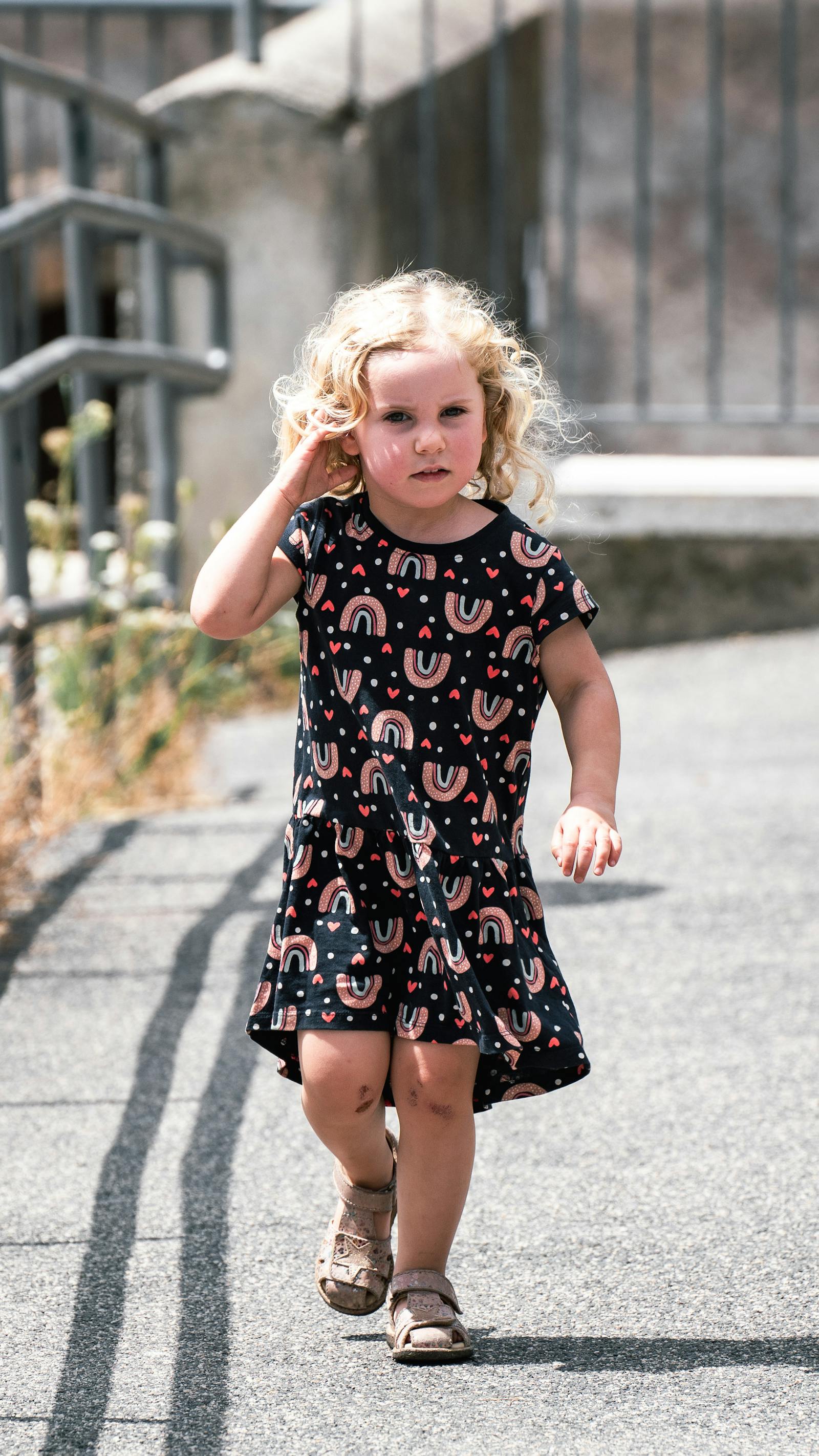 Blonde child in a sundress walking on a sunlit path in Rome, Italy, embracing carefree summer vibes.