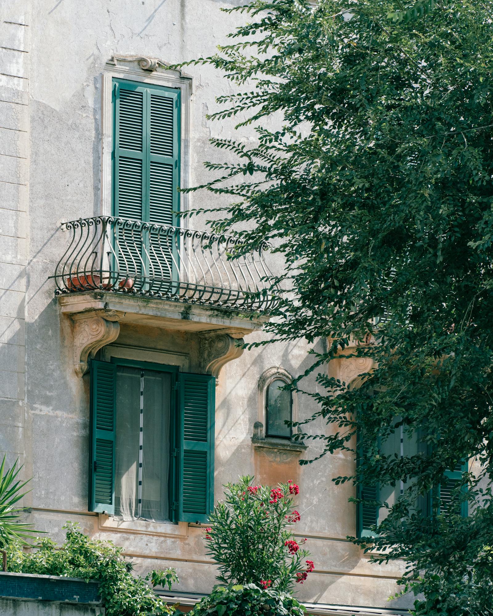 Captivating view of a traditional Roman balcony adorned with green shutters and lush plants.