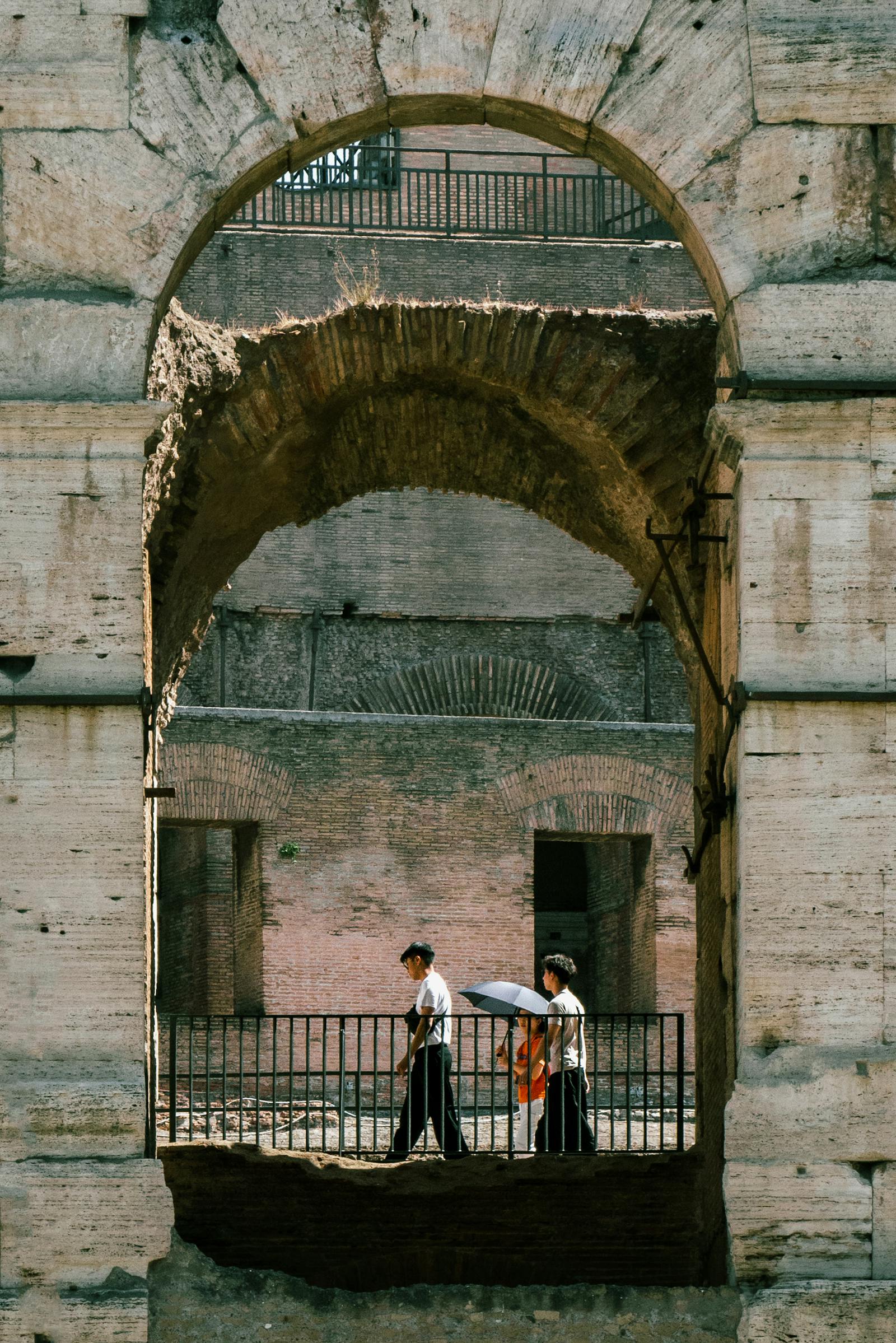 Two people walking through historic Roman arches at Colosseum in Rome, Italy.