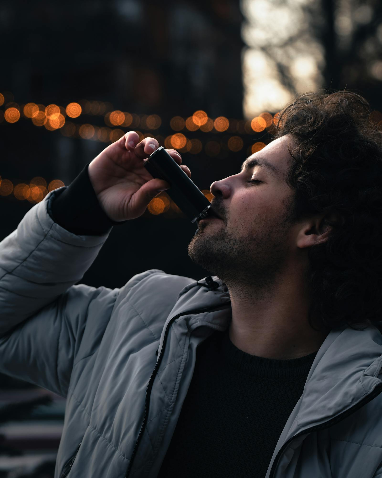 A stylish young man drinks from a bottle at an outdoor evening gathering in Thal, Austria.