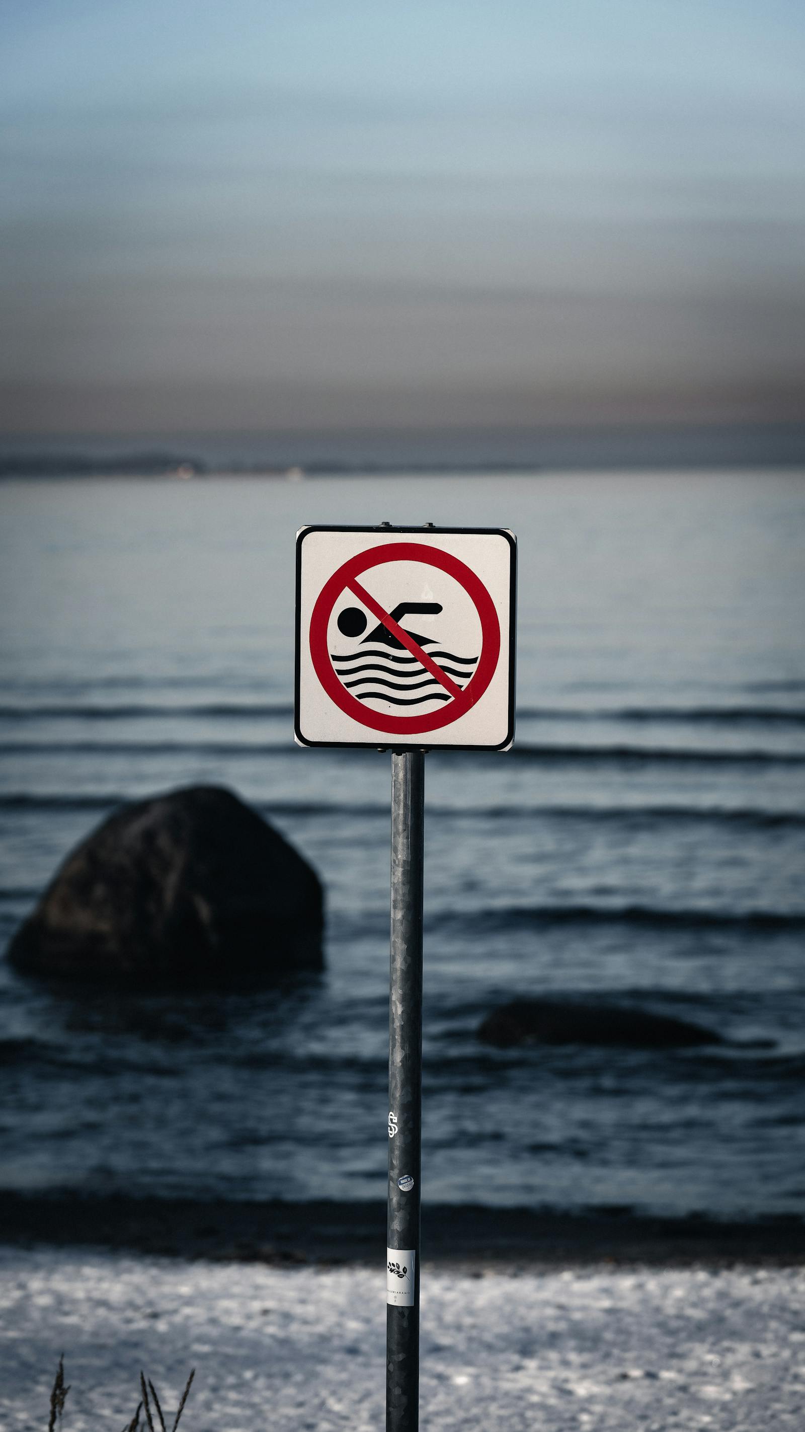 A no swimming sign stands by the sea on a serene Estonian beach at dusk.