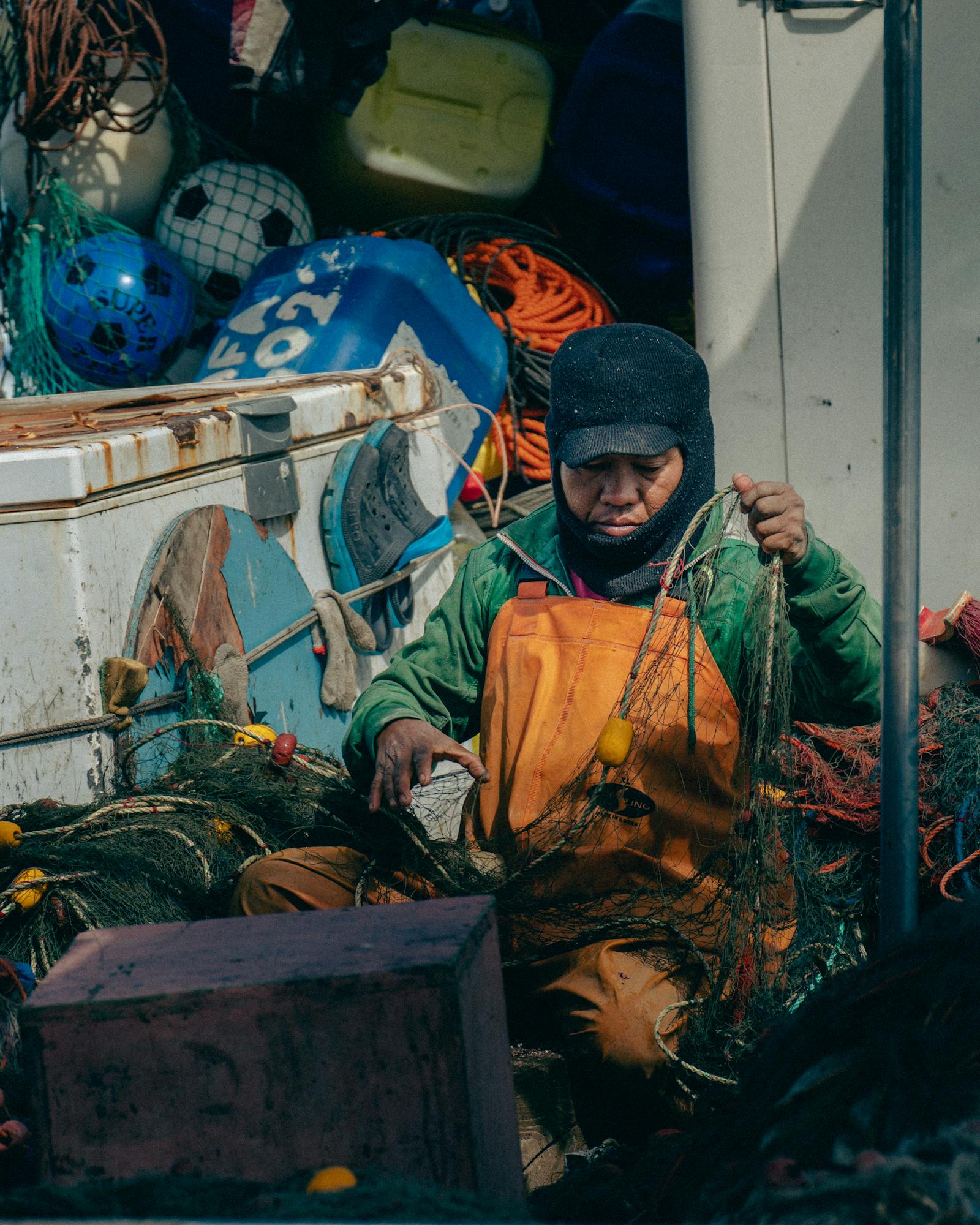 A fisherman tends to fishing nets on a boat, reflecting traditional fishing industry in Mellieħa, Malta.