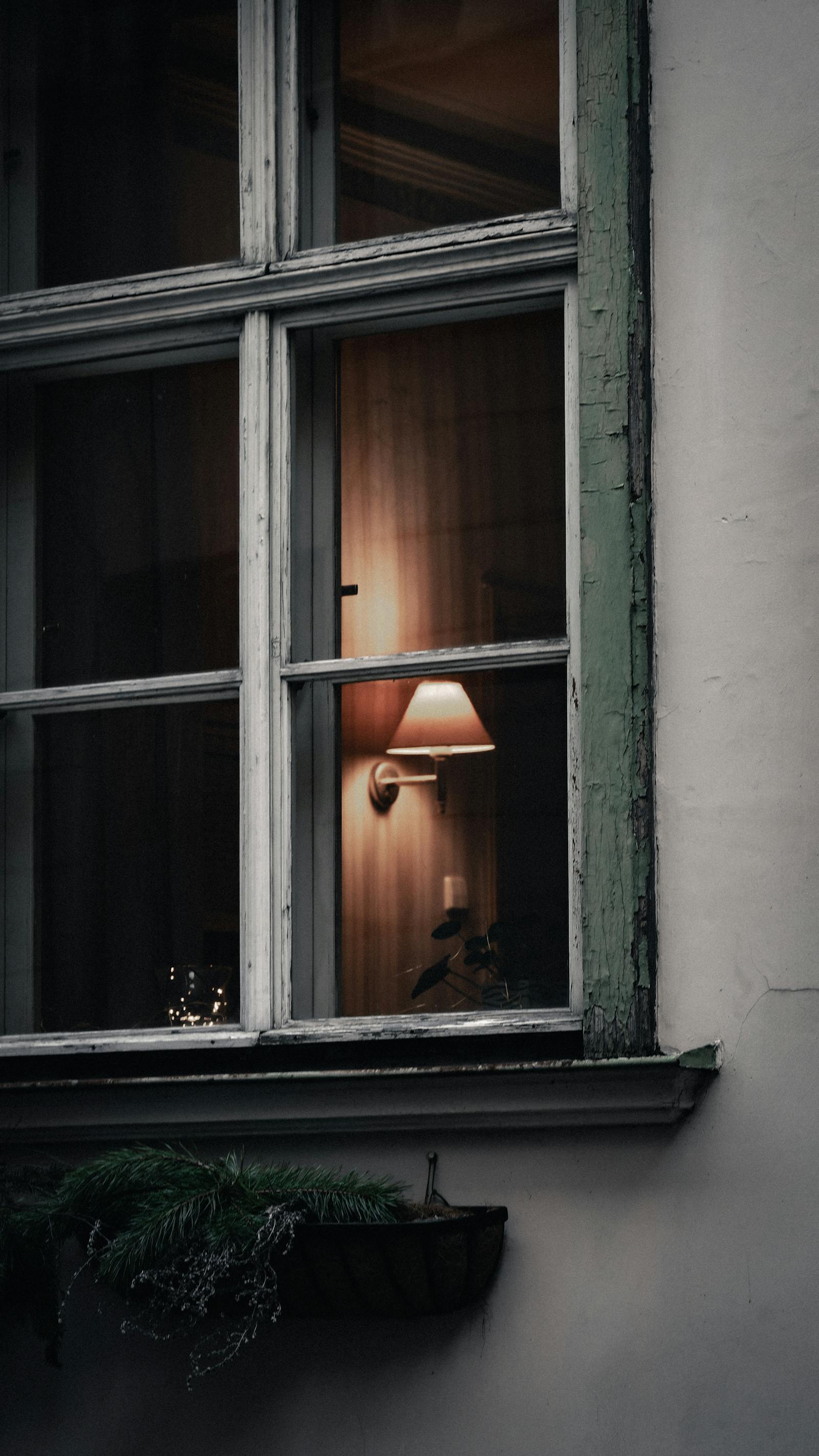 Warm light from a lamp viewed through an old Estonian window creates a cozy ambiance.