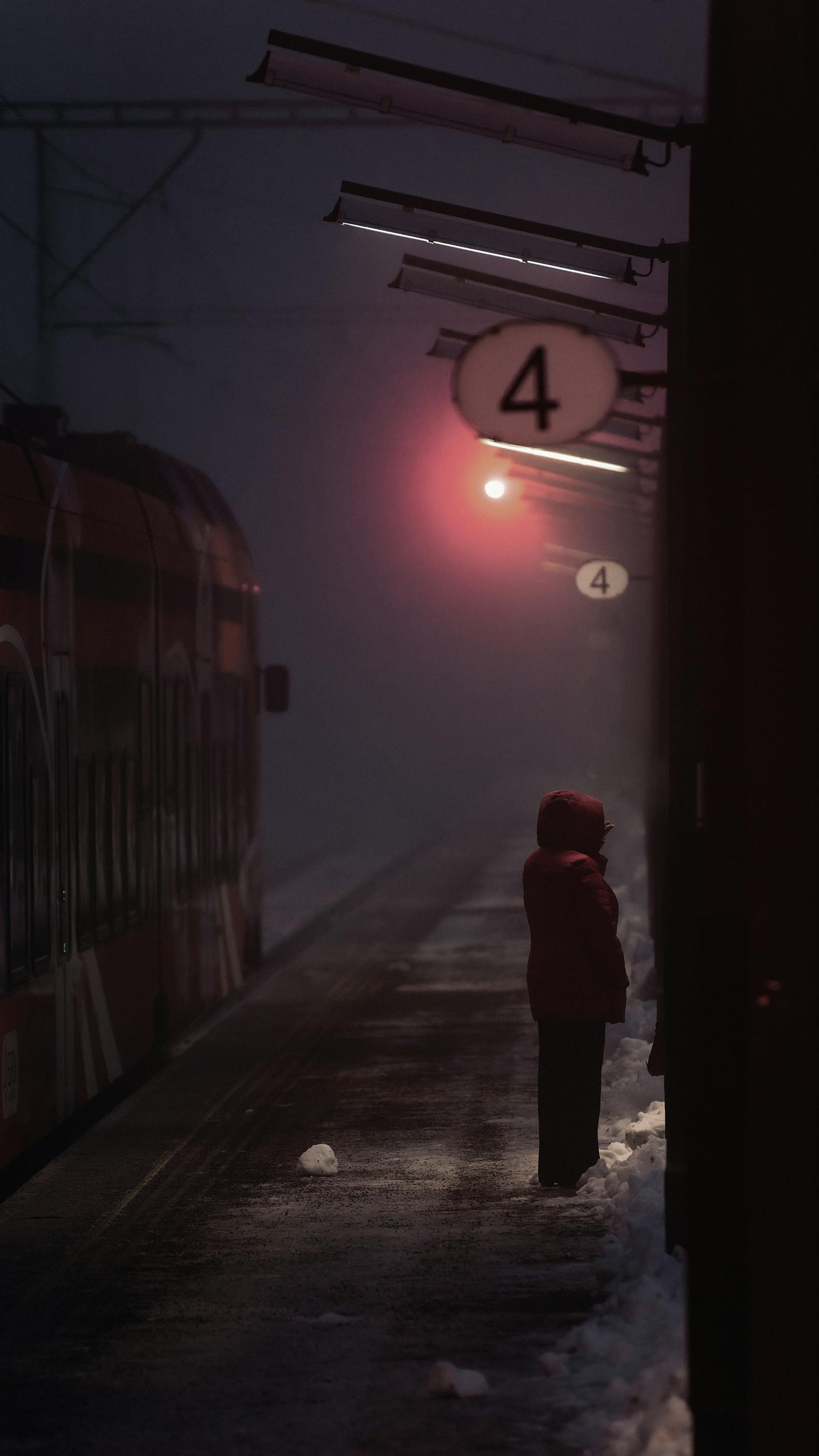 A person waits on a snowy railway platform at night in Estonia, highlighting winter travel.