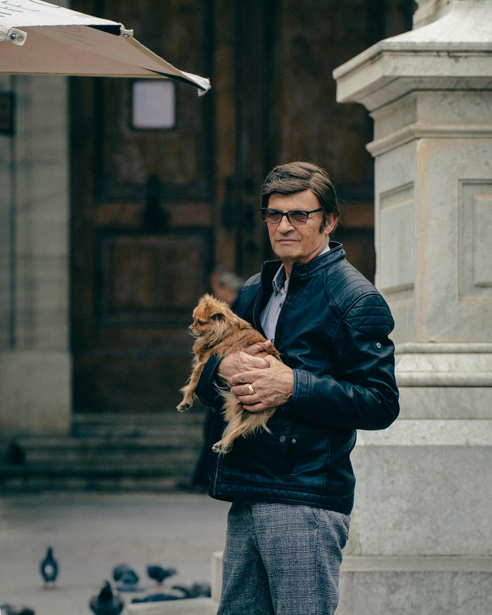 Man holding a dog in the streets of Valetta, Malta. Urban setting with a stone structure.