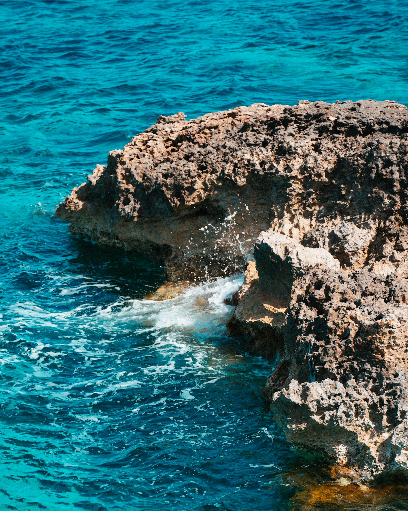 Stunning view of Malta's rocky coastline with crystal clear blue sea waves crashing against the rugged rocks.