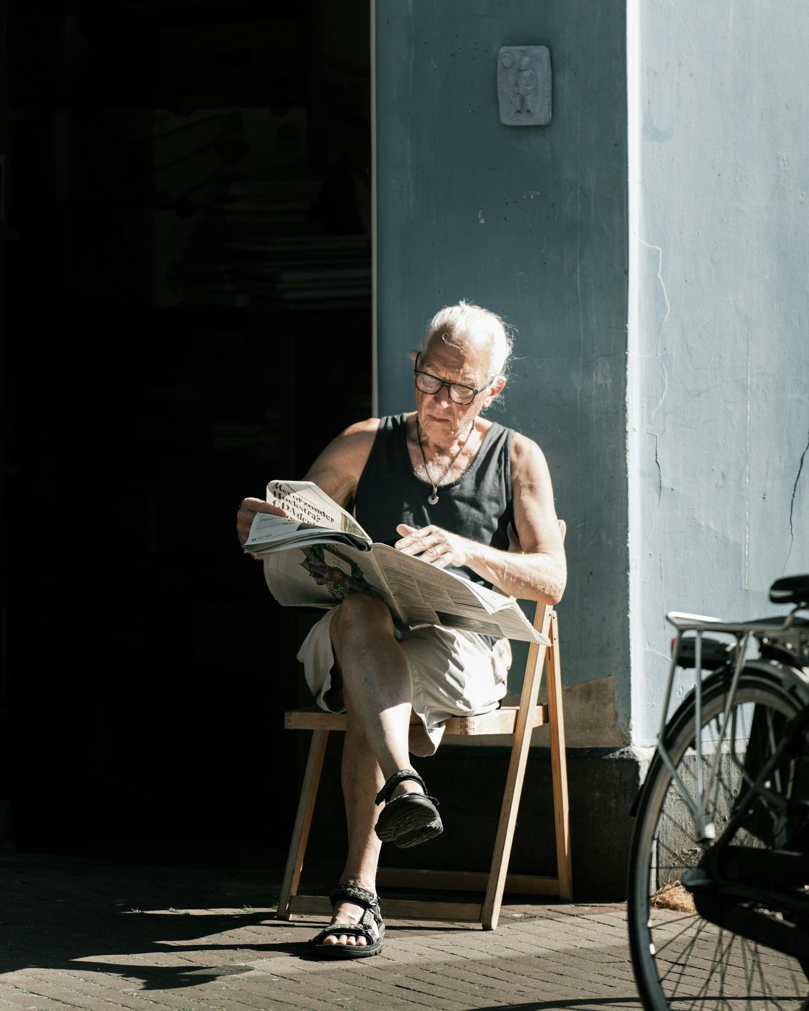 Senior man sits outdoors in summer reading a newspaper, enjoying the sunlight in Amsterdam.