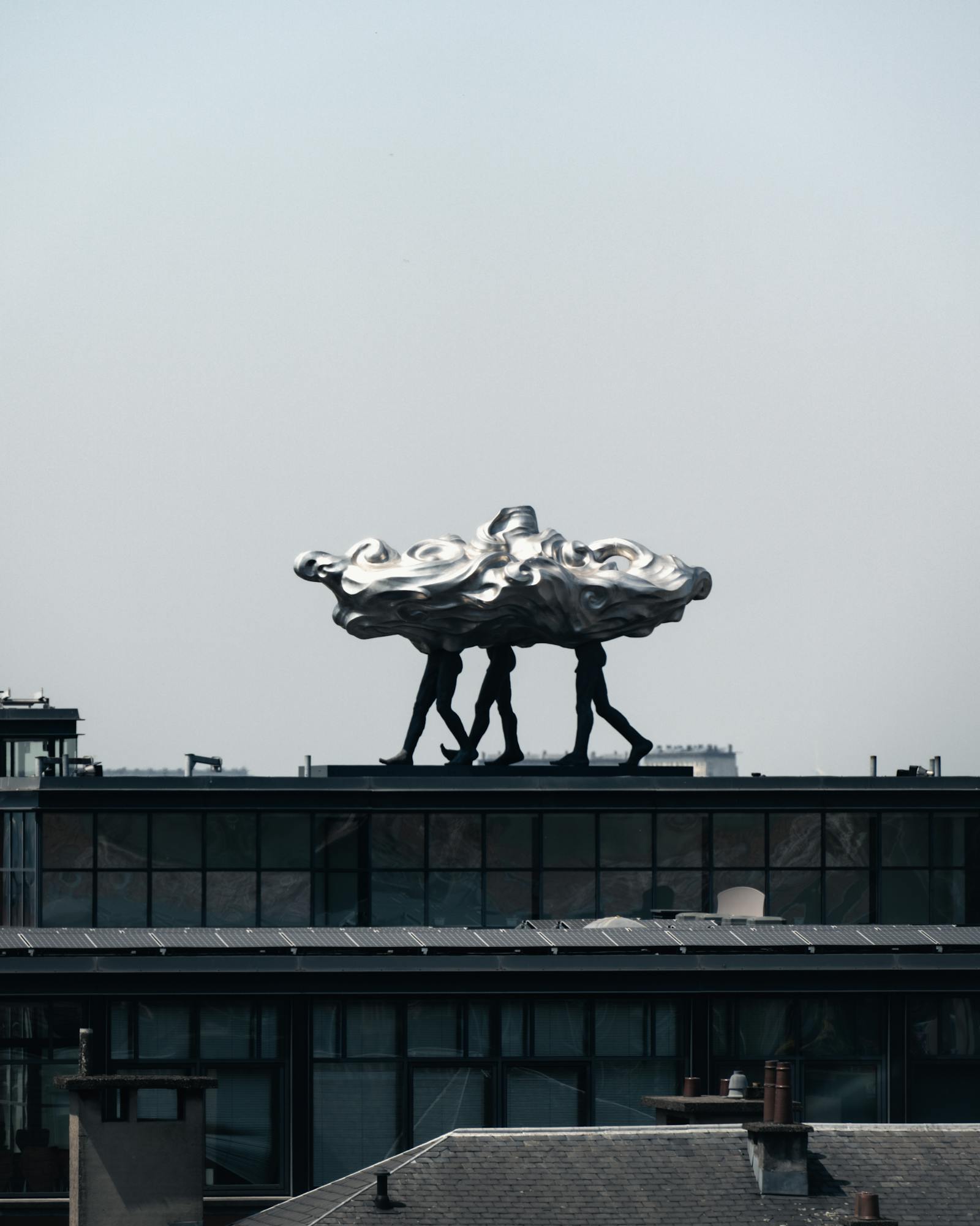 Artistic sculpture of figures on a Brussels rooftop, blending urban and modern aesthetics.