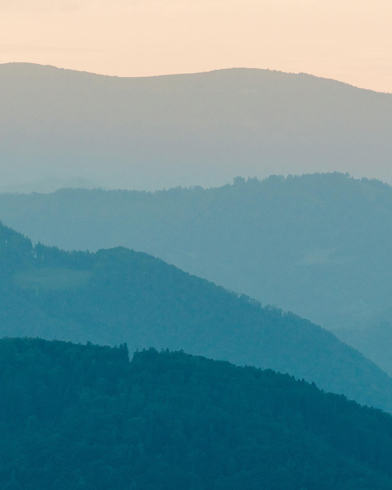 Serene aerial view of Graz hills with layered fog at sunrise.