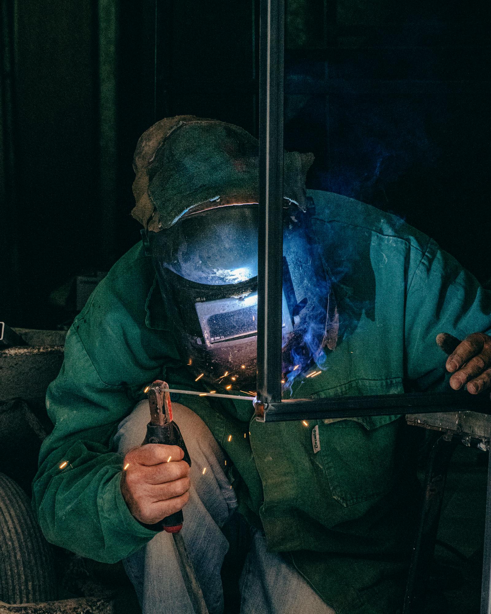 Welder using equipment in a Mellieħa workshop, garbed in safety gear with welding sparks.