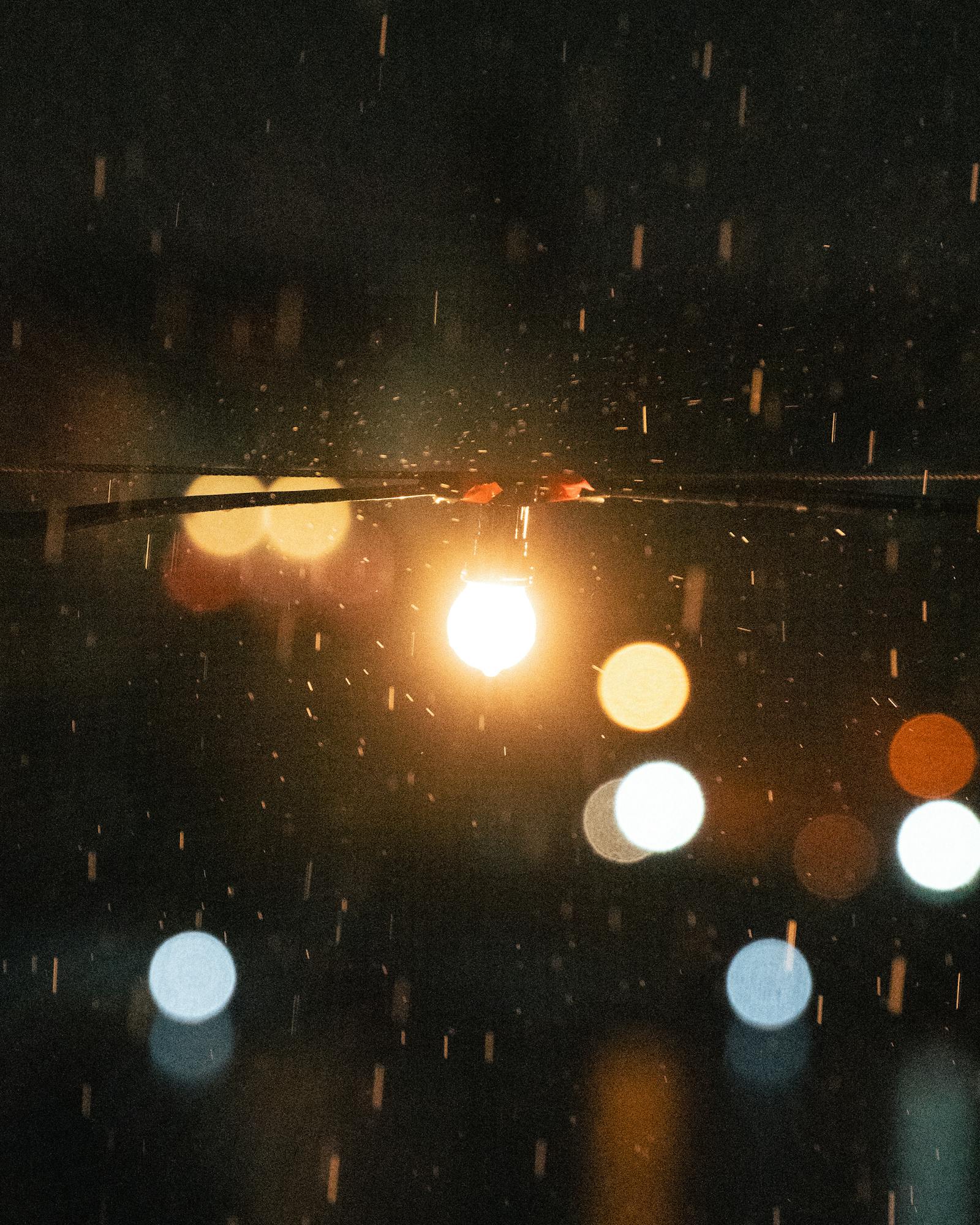 A moody evening shot of a glowing light bulb in the rain, enhanced by bokeh in Mellieħa.