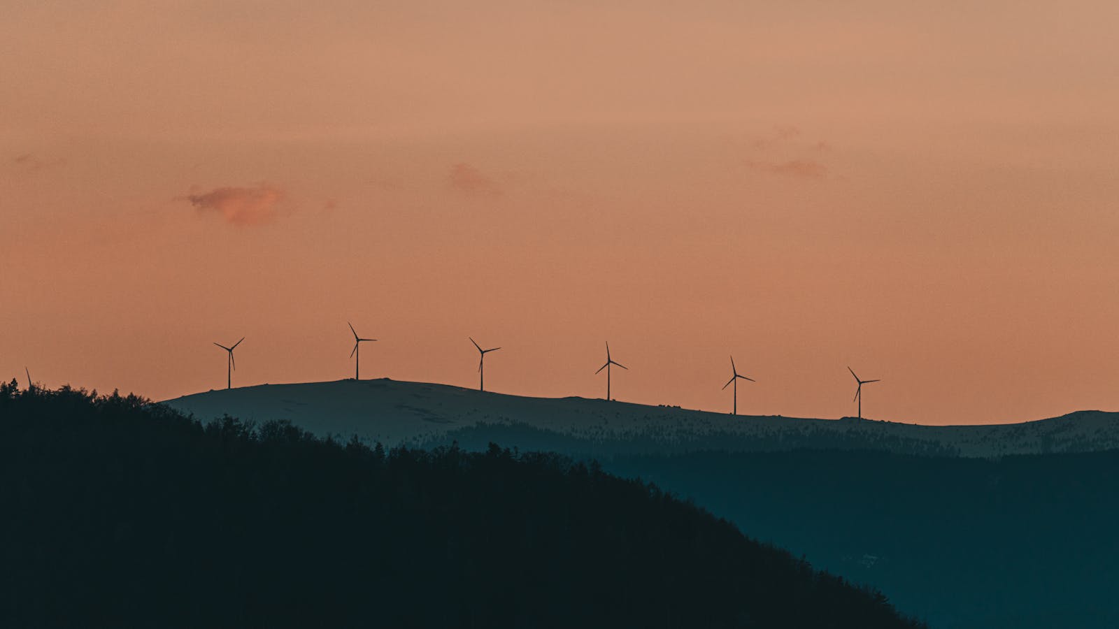 Wind turbines silhouette against a vibrant sunset in Graz, Austria.