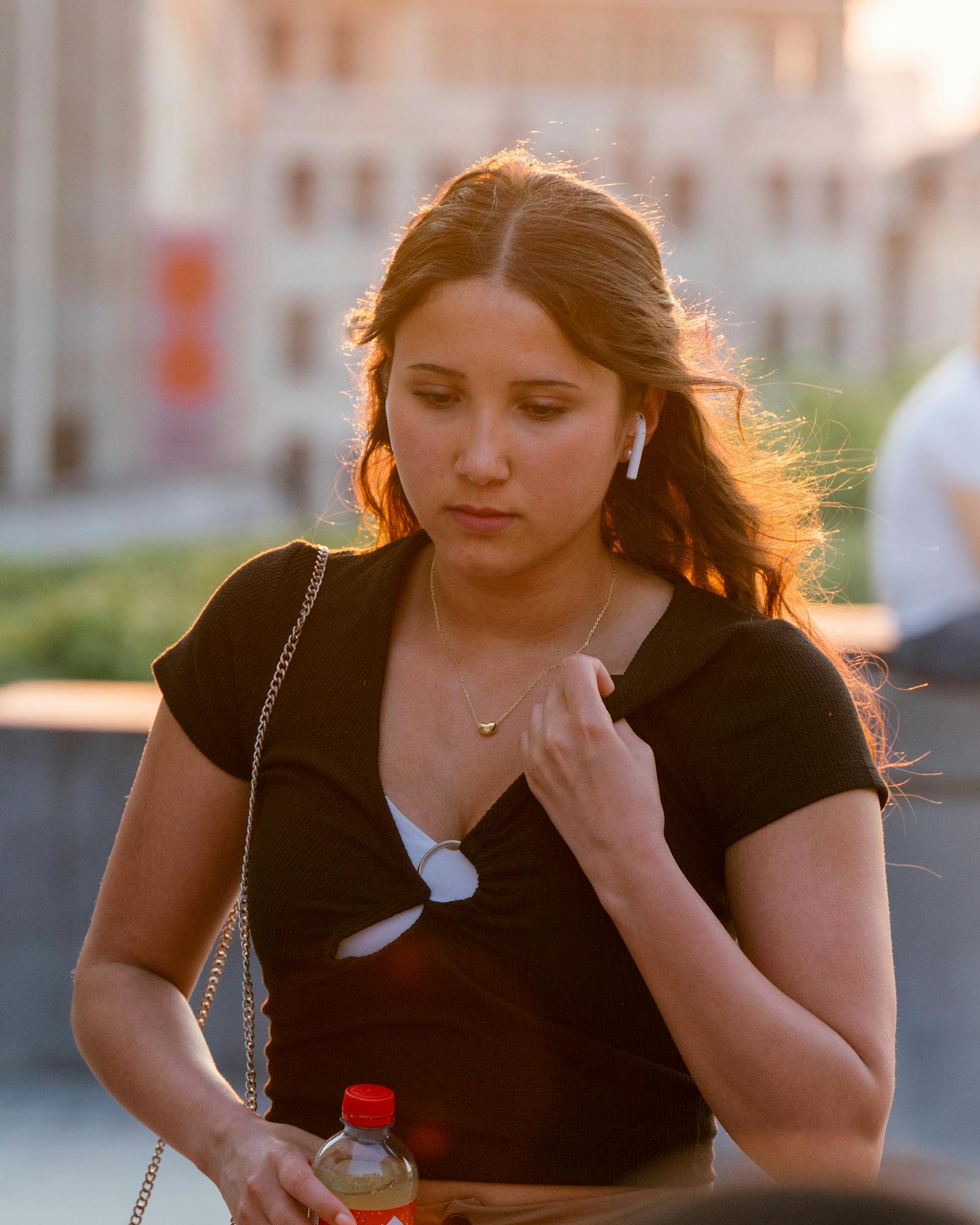 Portrait of a young woman with earbuds, walking outdoors in Brussels during sunset.