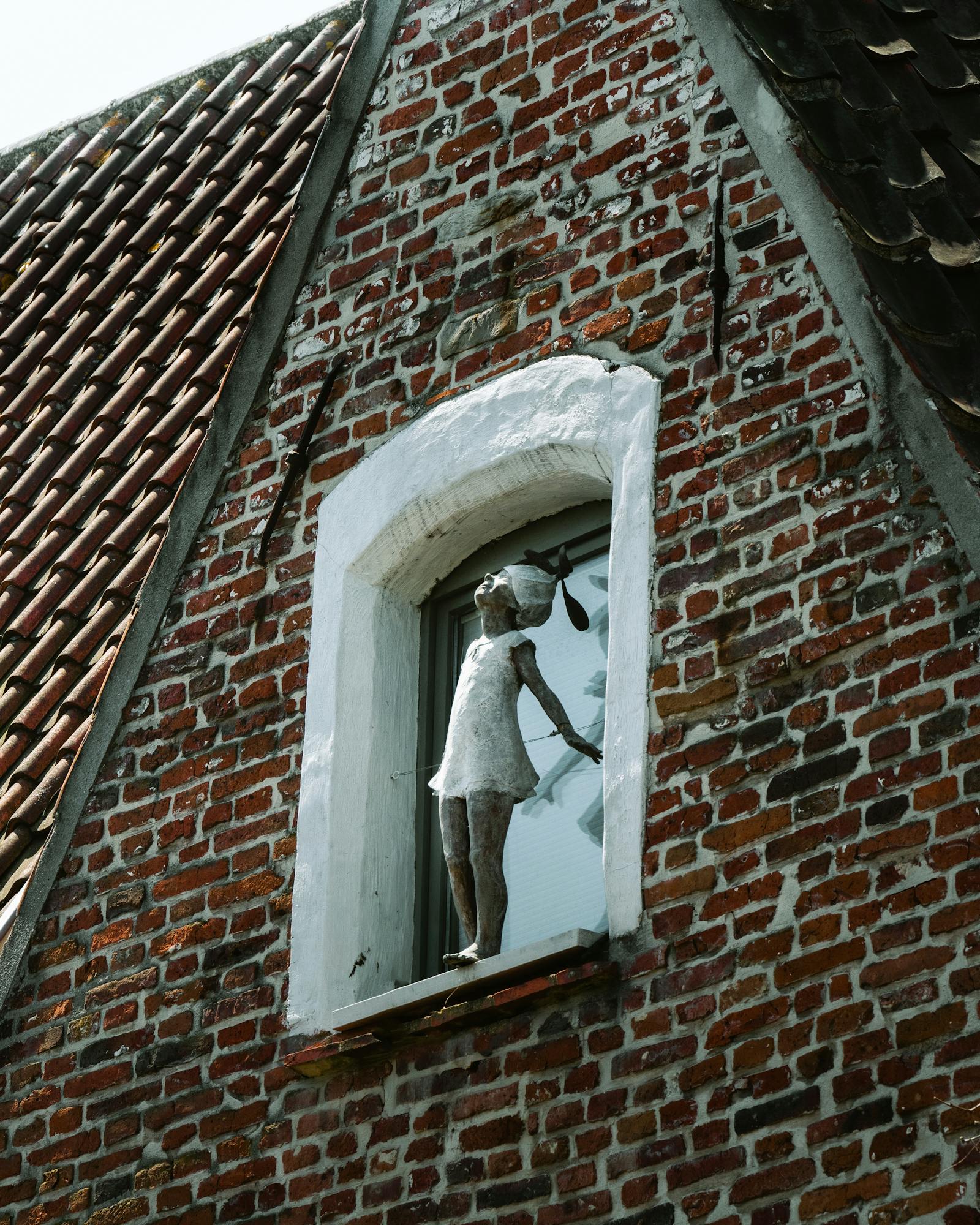 A vintage facade with a sculpture in a window in Ghent, Belgium.