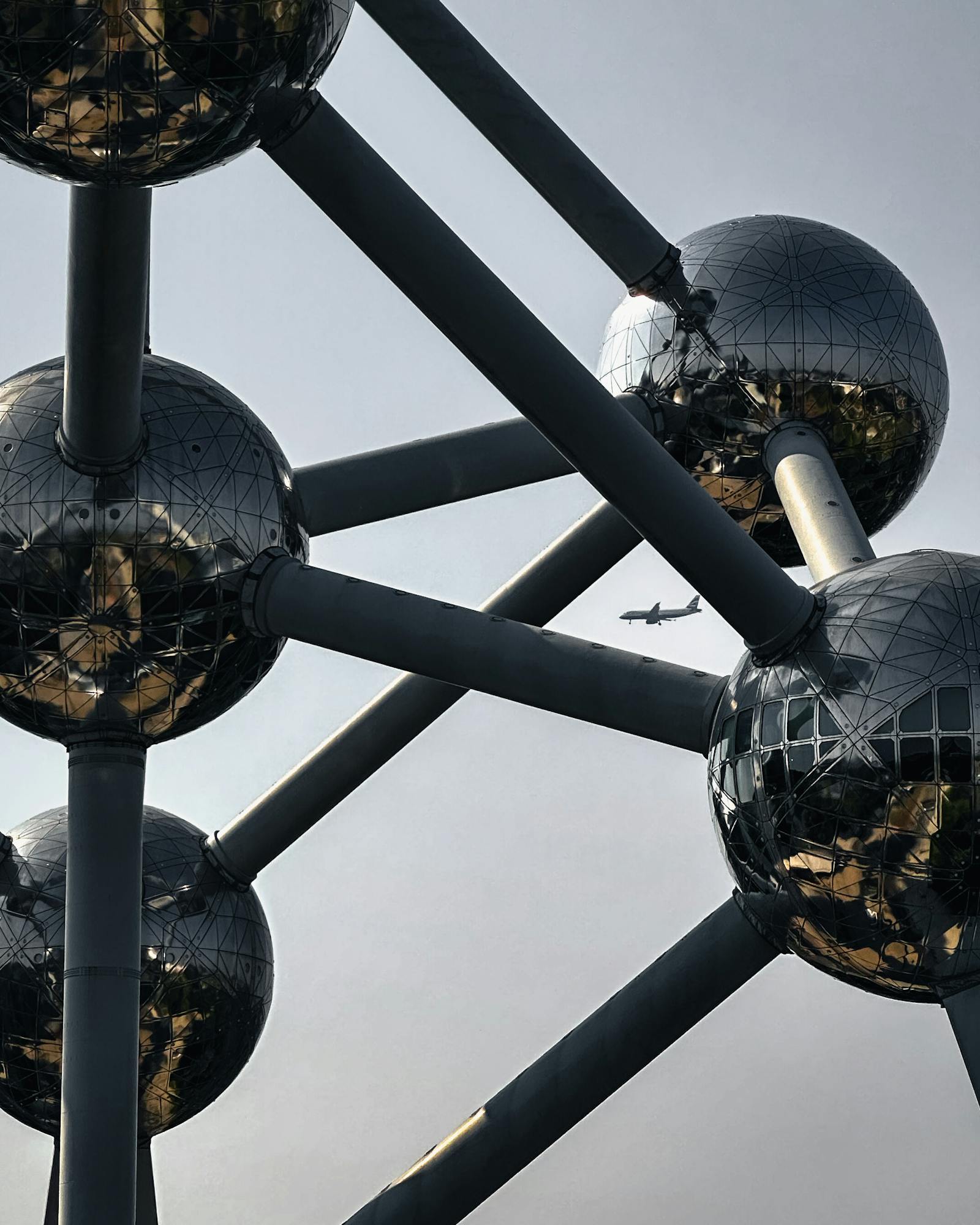 Close-up of the Atomium structure in Brussels with an airplane in the sky.