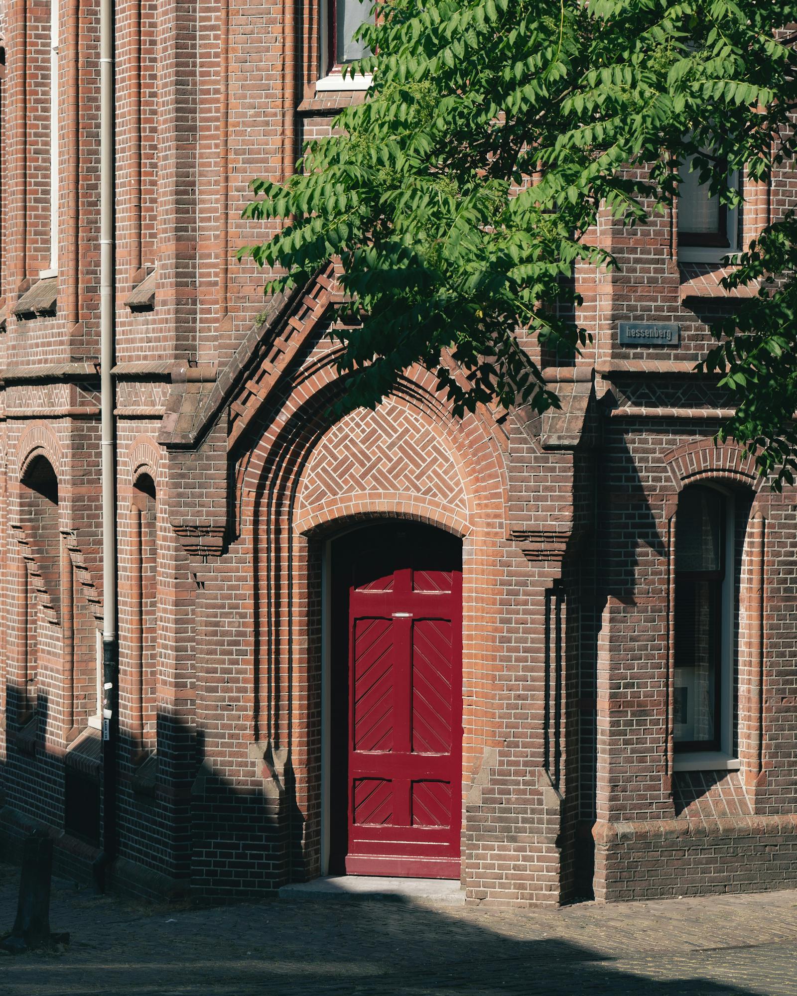 Elegant 19th-century brick building with arched red door and tree shadows.