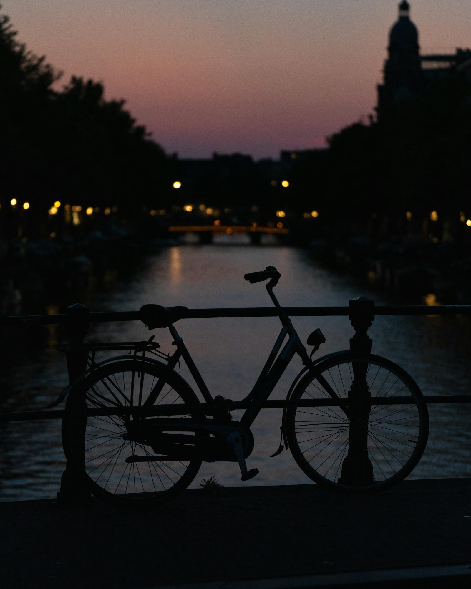 Silhouette of a bicycle on an Amsterdam canal bridge at sunset.