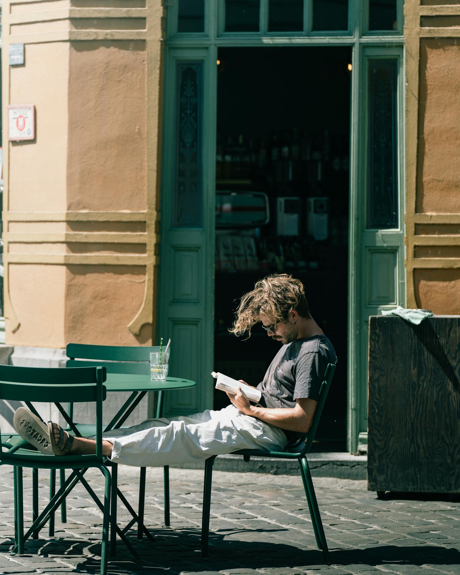 A man reads a book outdoors at a sunlit cafe in Gent, Belgium.